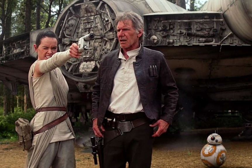 Rey aims a pistol as Han Solo gives her instructions.