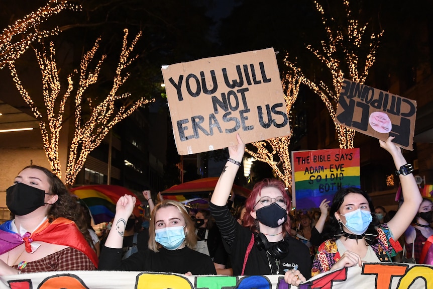 A group of protestors hold a sign which reads 'You Will Not Erase Us.'