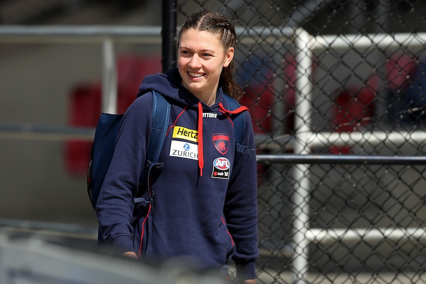 An AFLW player smiles as she walks through the gate to a football ground ahead of a game.