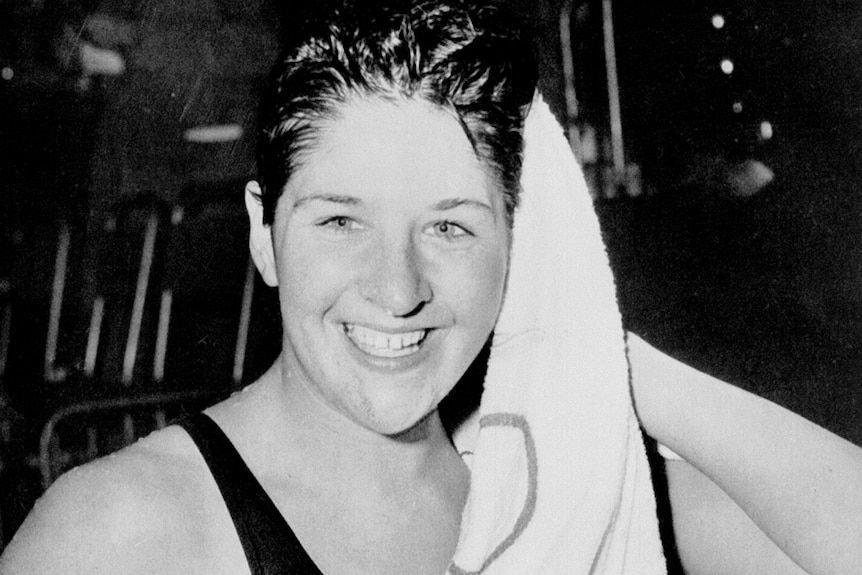 An Australian female swimmer dries her hair after a swim and smiles in 1960.