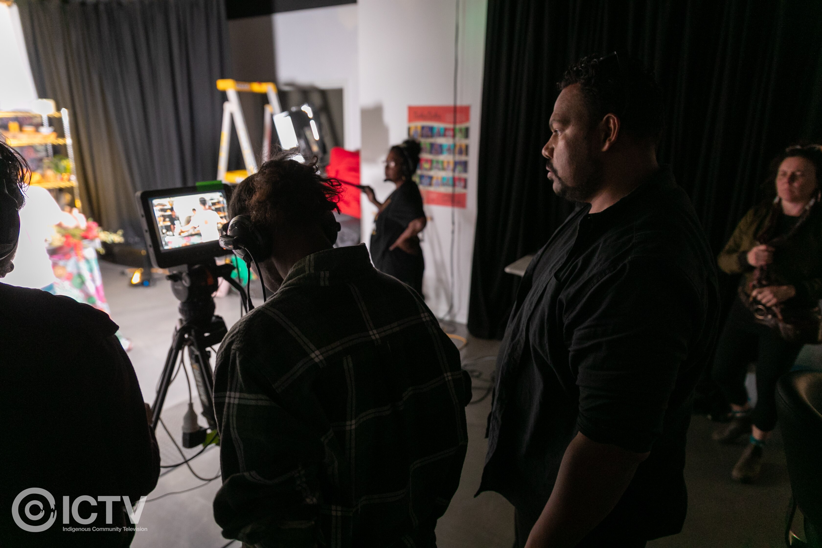 Man looking at ipad screen on tripod as sound and camera people operate equipment in TV studio.