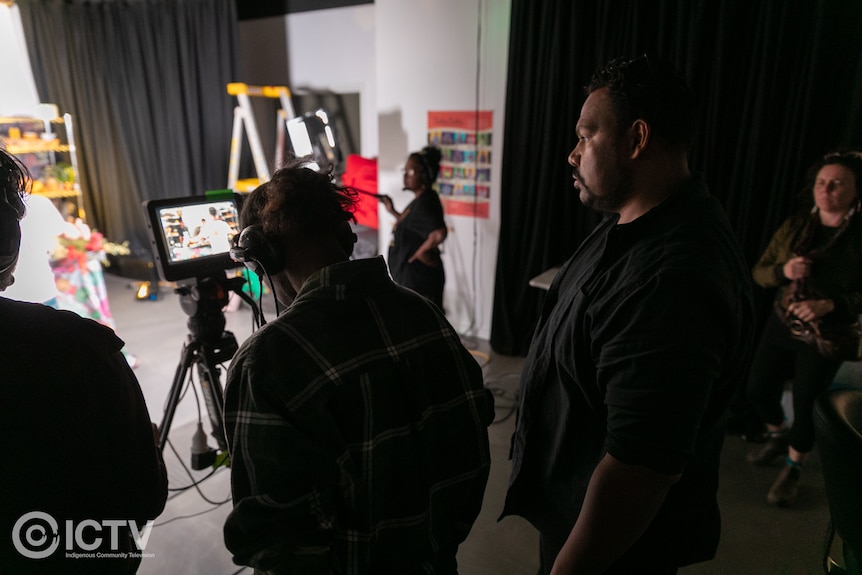 Man looking at ipad screen on tripod as sound and camera people operate equipment in TV studio.