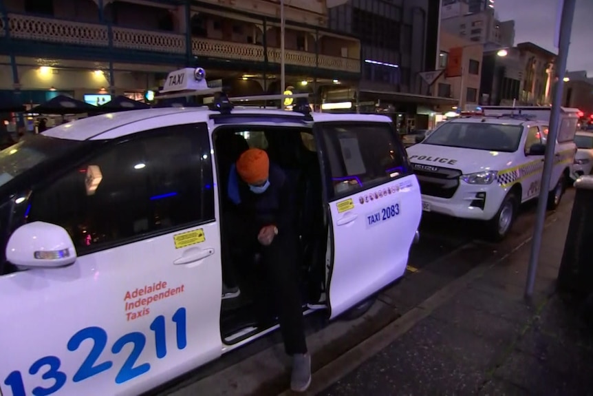 A man wearing an orange turban enters a van with taxi markings