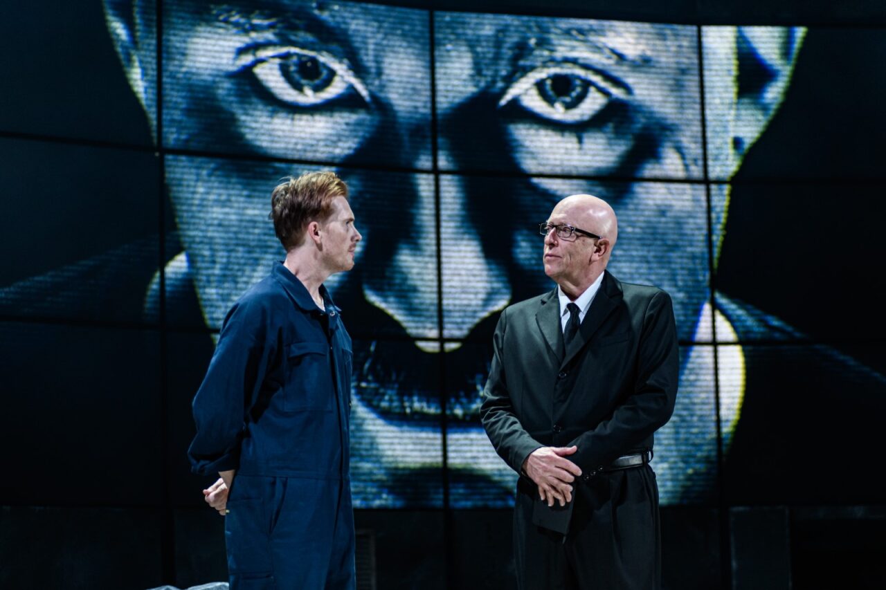 Actors perform under the watchful eyes of giant Big Brother wallpaper.