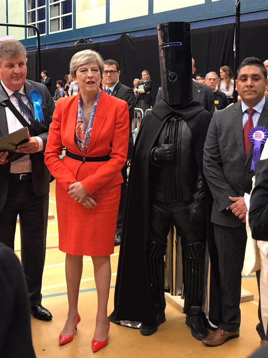 Theresa May stands next to Lord Buckethead — a person cloaked in black with a bucket on their head — during the UK election.