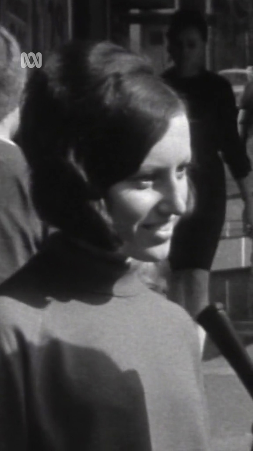 A black and white image shows a young woman with short hair smile as she faces off camera