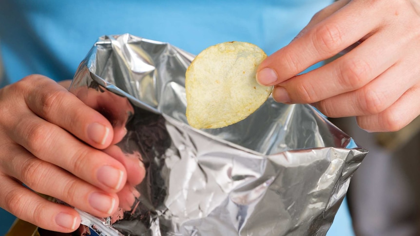 The girl takes crispy fried fatty potato chips from a pack