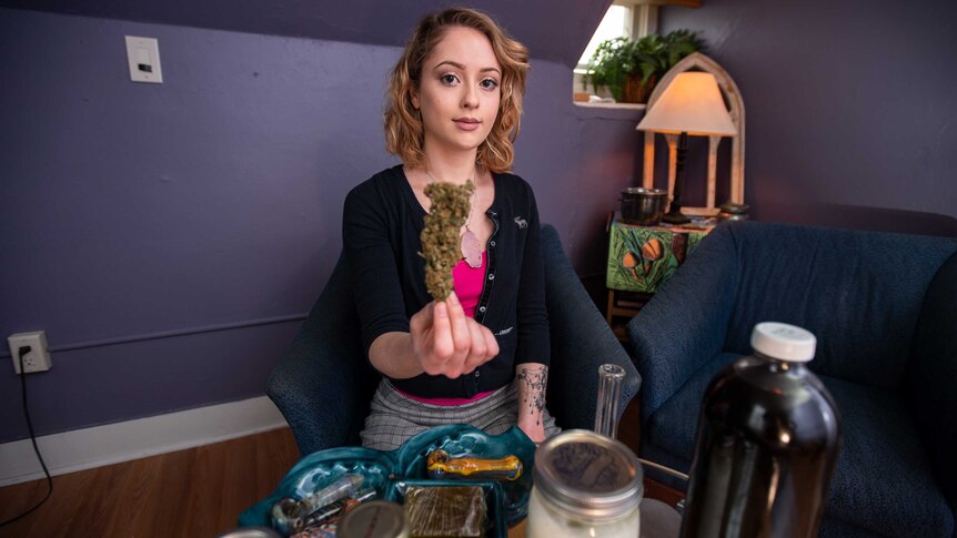 A young woman holds up a marijuana bud