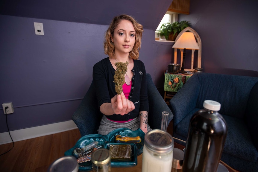 A young woman holds up a marijuana bud