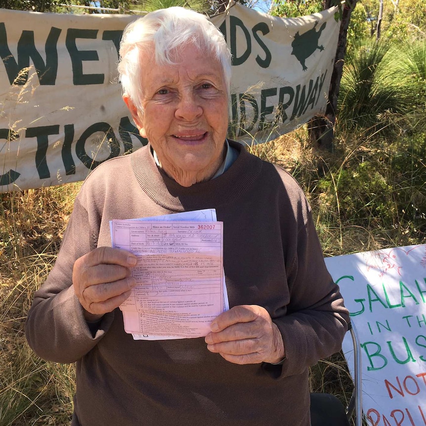 Val Oliver holds up pieces on paper standing in front of banners outdoors.