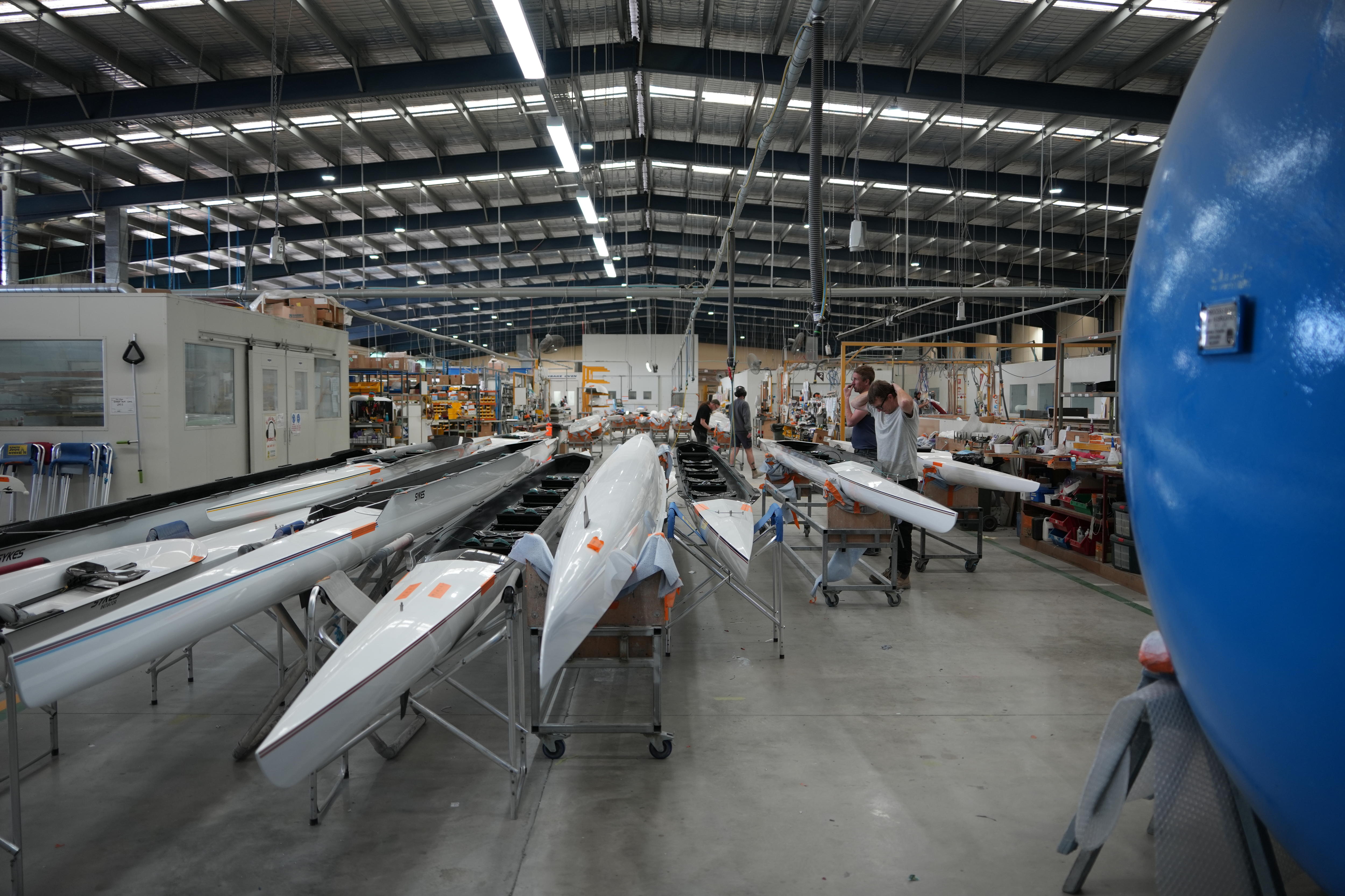 Grey rowing boats lined up on stands inside a large shed or warehouse.