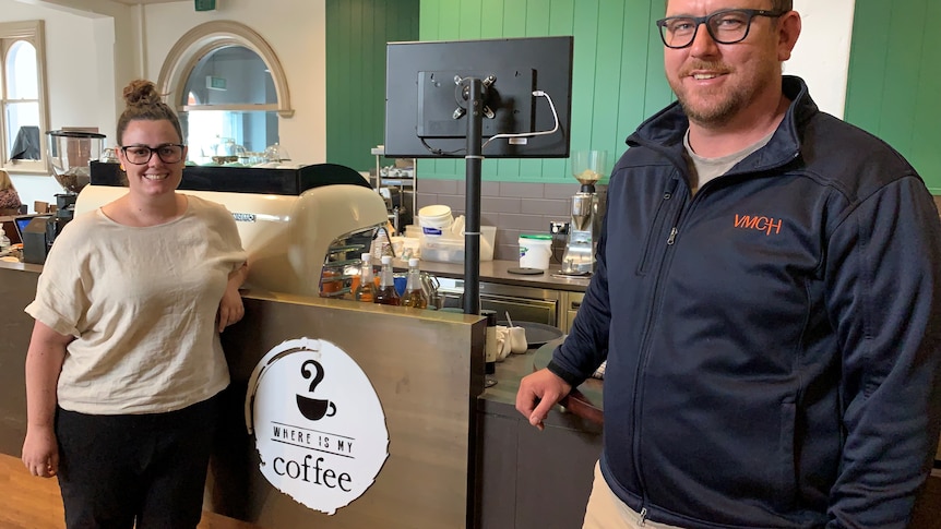 Woman and man smiling stand in front of a coffee shop counter