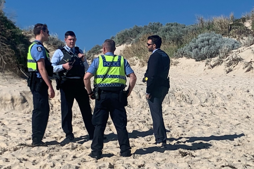 Four police officers stand talking to each other on a beach