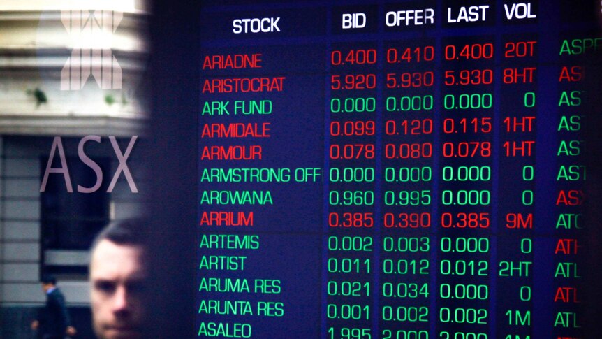 A man's face is reflected in the window of the Australian Securities Exchange. Inside a board is lit with various falling stocks