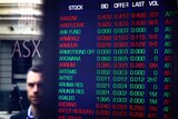 A man's face is reflected in the window of the Australian Securities Exchange. Inside a board is lit with various falling stocks