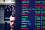 Pedestrians reflected in the window of the Australian Securities Exchange next to a board displaying stock prices in Sydney