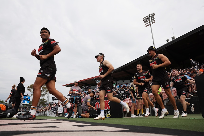 A Penrith Panthers NRLW player runs out on the ground in training gear, followed by teammates as a big crowd watches on. 