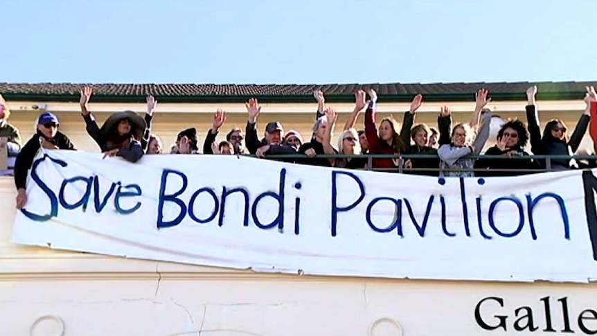 A group of people hold a banner reading 'save Bondi pavilion.'
