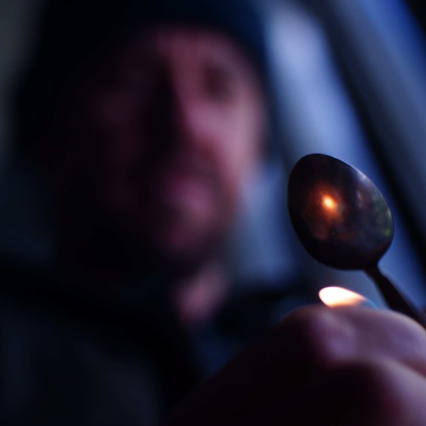 A man heats something up in a metal spoon.
