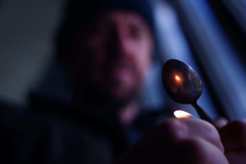 A man heats something up in a metal spoon.