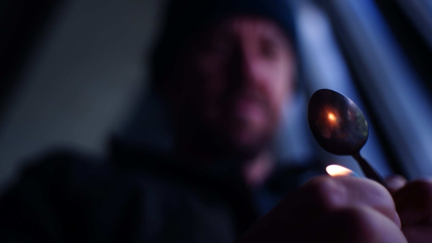 A blurred man holds a lighter under a spoon