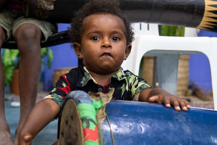 A small boy bangs on a drum.