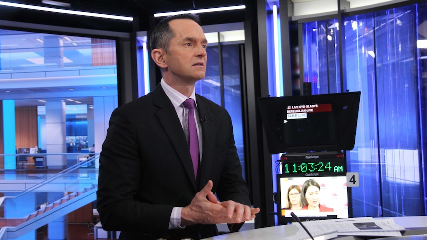 O'Brien sitting at desk in studio with camera to his left.