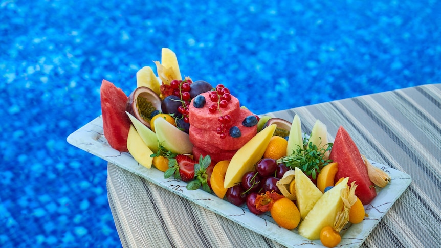 A fruit platter with watermelon, passionfruit, pineapple by a pool, cut up fruit for summer sharing.