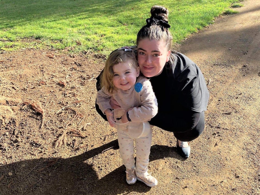 A woman in a park with a child smiles at the camera