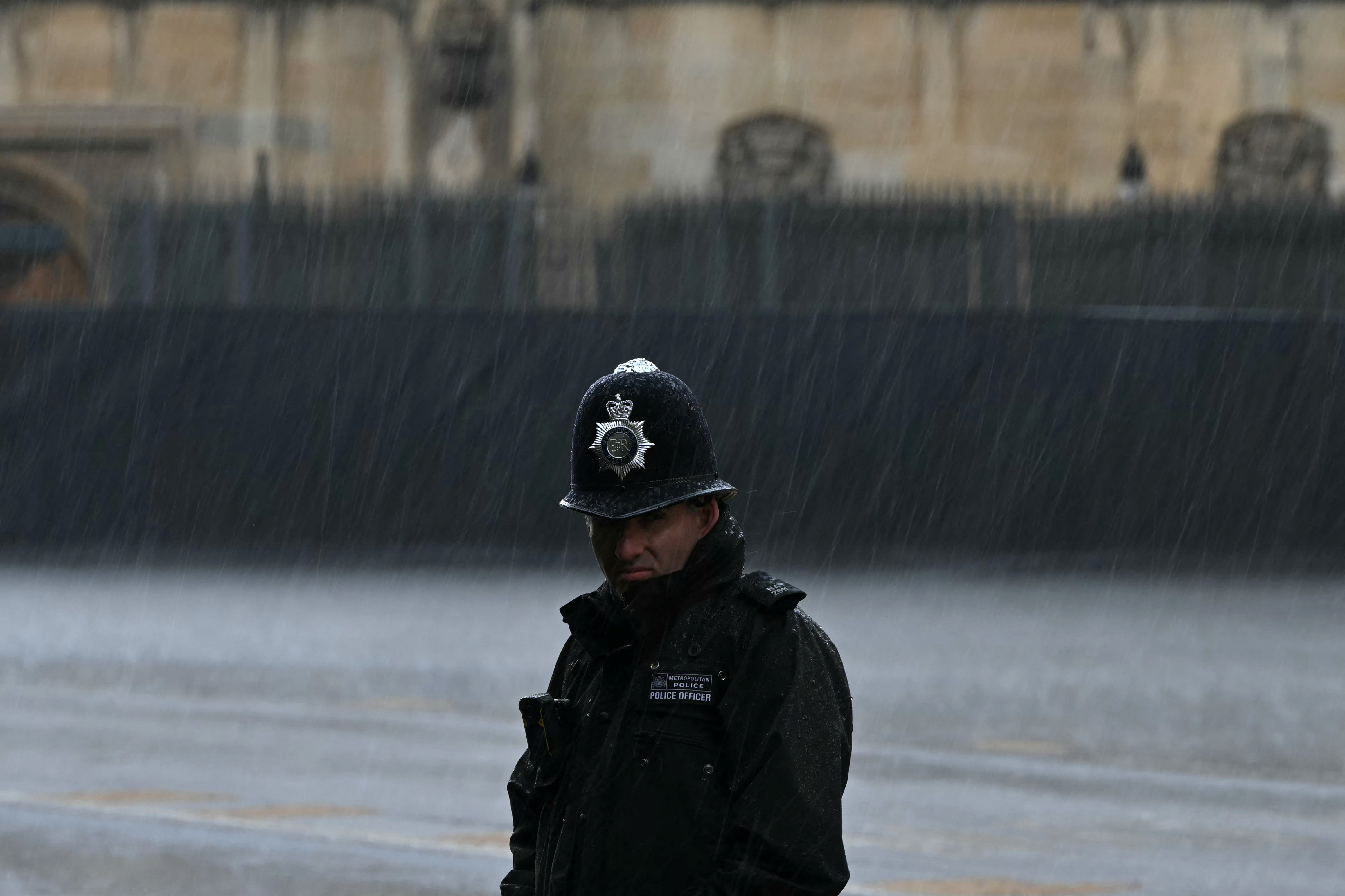 A Metropolitan Police Officer standing in the rain, on a blurred background.