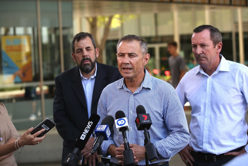 Roger Cook speaks to the media while Andrew Robertson and Mark McGowan stand behind him.