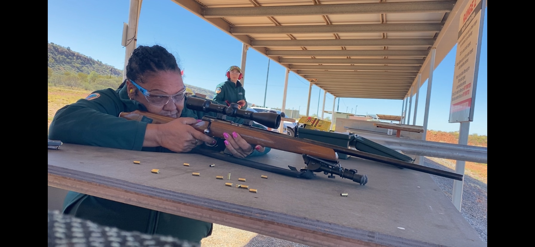 A close up shot of an Aboriginal women squinting as she lines up a shot. She has hot pink finger nails.