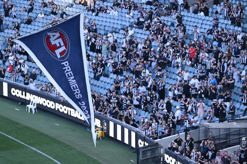 A large blue flag with the AFL logo on it and "premiers 2023" flies above the MCG, with Collingwood fans in the stands.
