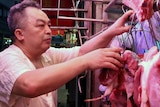 A vendor touches a piece of meat hanging from a hook at a market