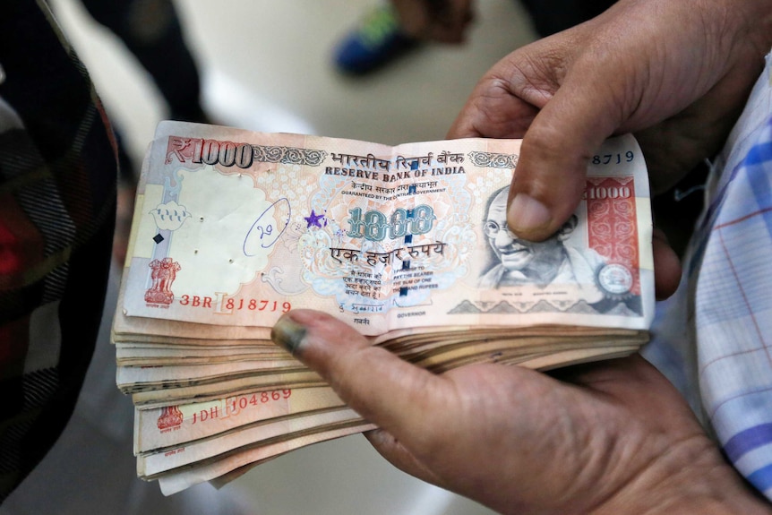 A customer waits to deposit 1000 Indian rupee banknotes.