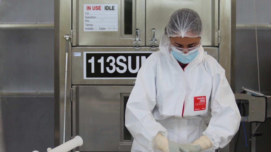 A woman in a hairnet, mask and protective suit holding plastic pipes in a lab