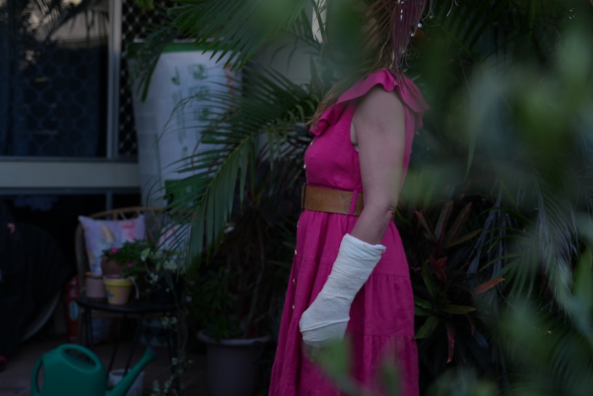 A woman in a pink dress and bandaged arm in a garden
