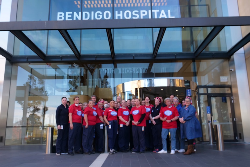 A group of nurses stand in front of a hospital entrance