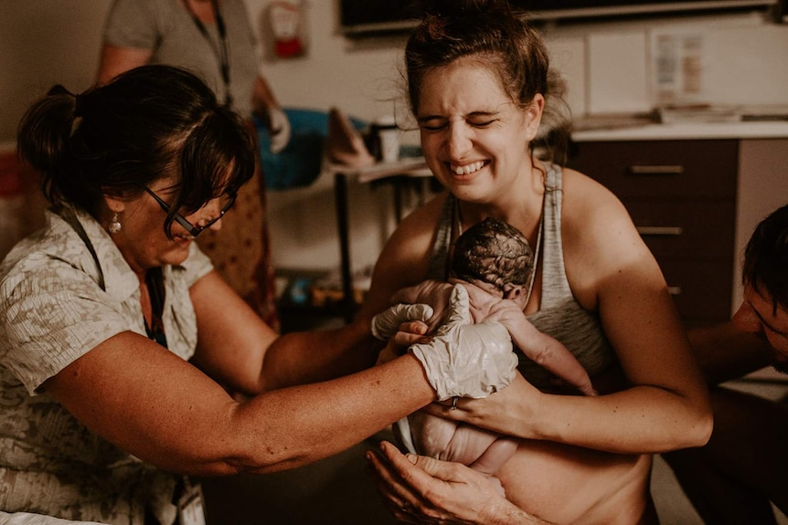 A young wwoman is handed her newborn baby in a hospital room.