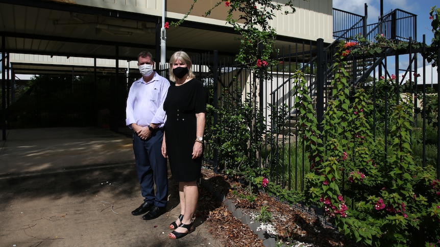 A man and a woman stand in masks in front of a defective Palmerston house.