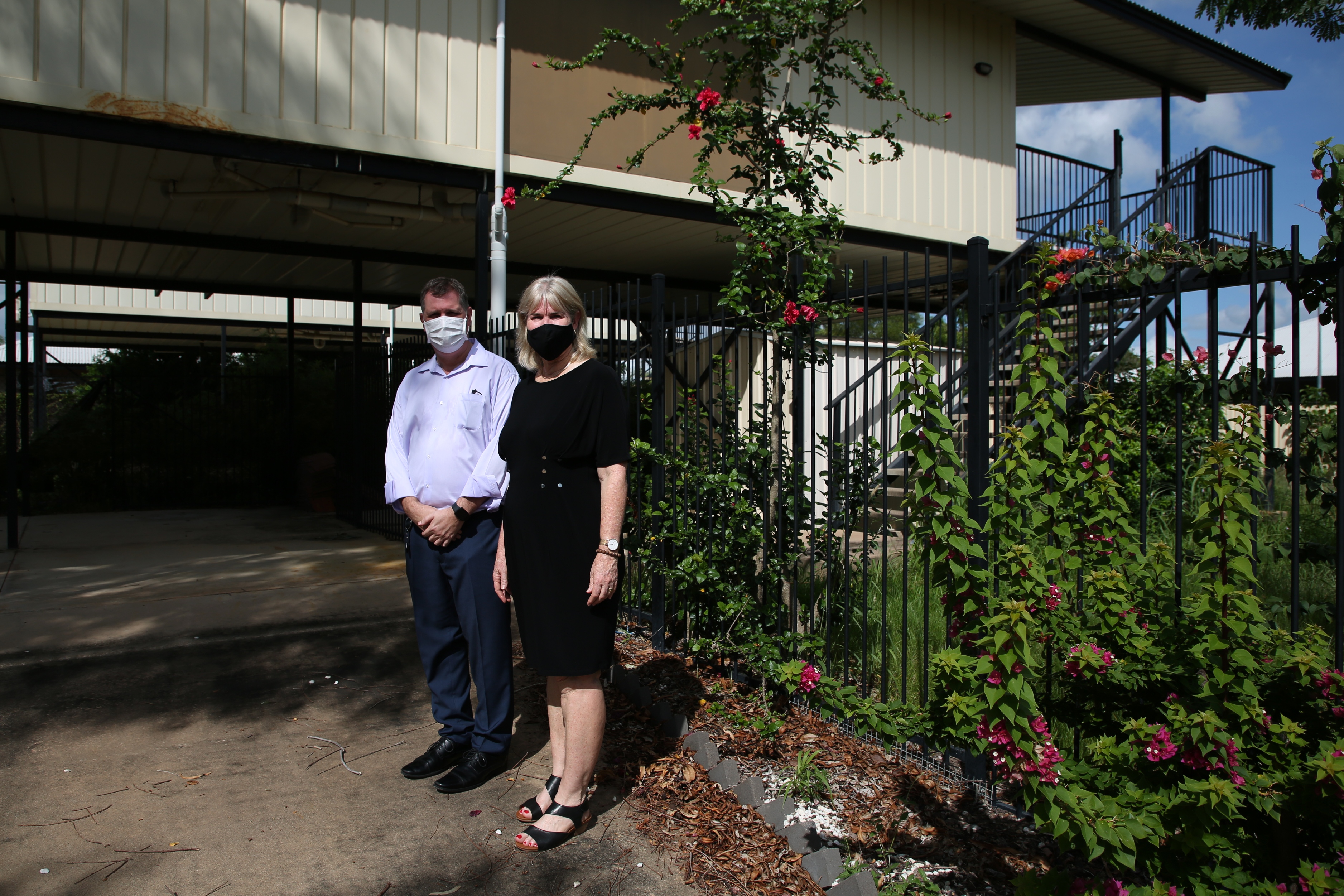 一男一女戴着面具站在有缺陷的帕默斯顿房子前。