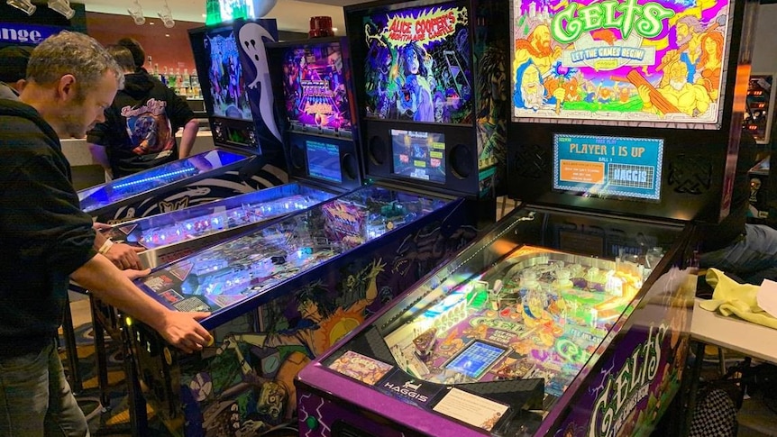 A man playing a pinball machine and in the foreground an Australian-made pinball game called Celts.
