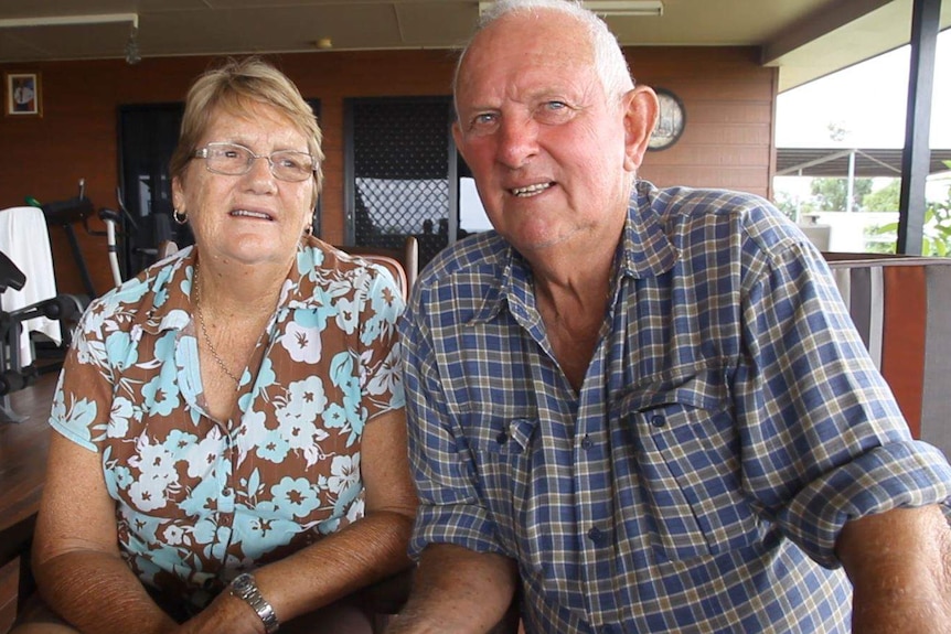 An older couple sit next to each other on a big deck in a rural setting.