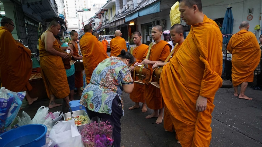 A woman bows to a group of men with shaved heads and dressed in saffron robes
