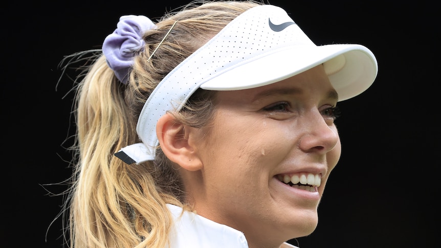 A female tennis player wearing a white hat cries