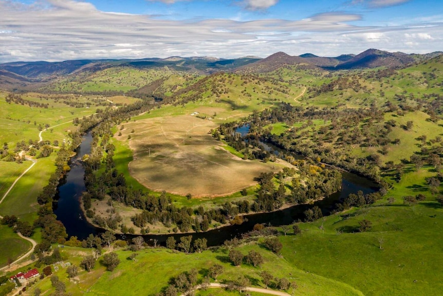 Green hills with a river bending around he hills and trees.