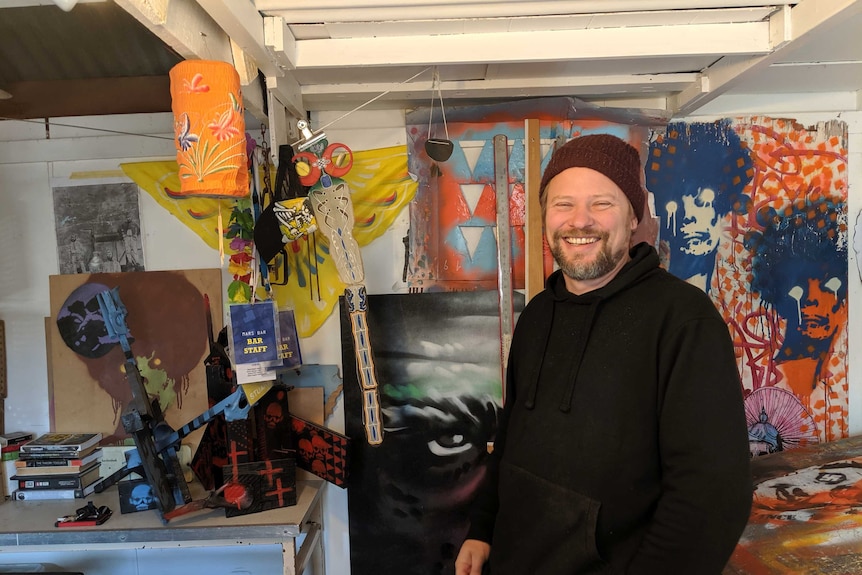 A smiling man in a studio filled with his graphic art