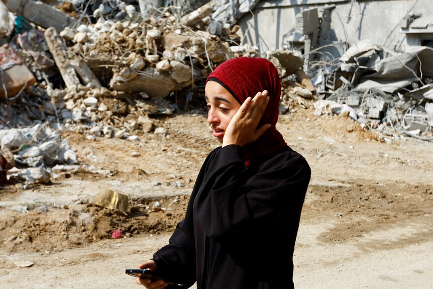 A woman in a headscarf clutches her face near rubble 