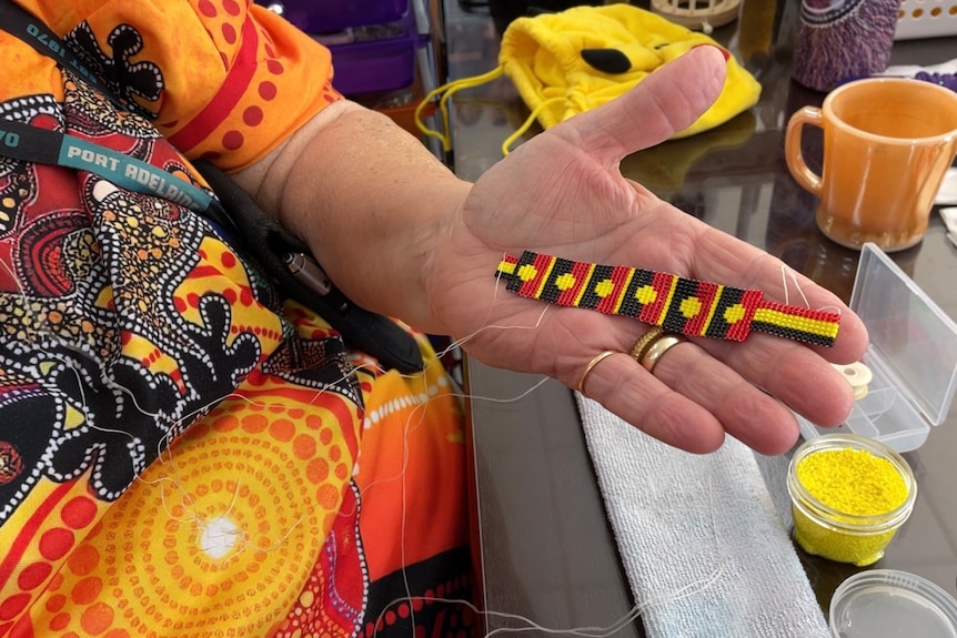 A woman's hand holds a beaded bracelet with designs of red, black and yellow aboriginal flags.  