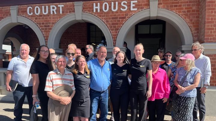 A large group of people stand outside a historic-looking court building.